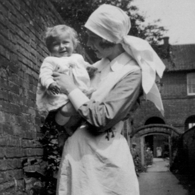 Nurse Eileen Olive Woods standing outside in her nursing uniform holding a baby