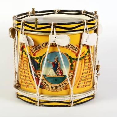 Side-view of a yellow snare drum. The drum is decorated with the Royal Norfolk Regiment's insignia - a painting of Britannia. Text on the drum reads 