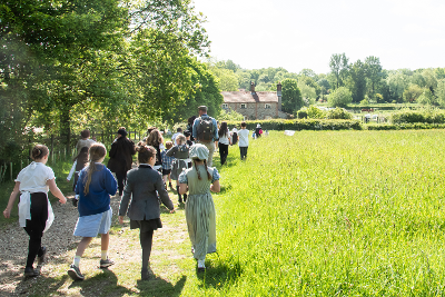 Children in costume being led through a field by an adult